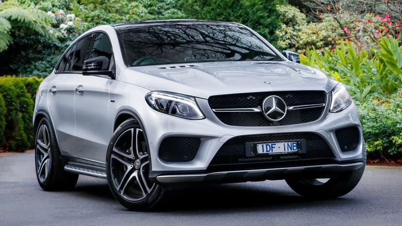 Silver Mercedes-Benz GLE Coupe parked on a driveway surrounded by green garden foliage and trees.