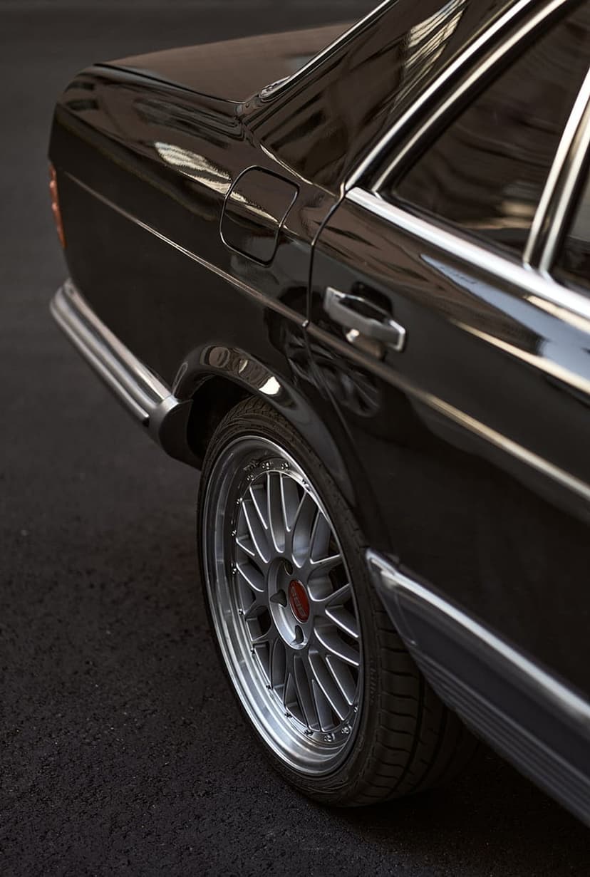 Mercedes alloy wheel and chrome trim on a black classic sedan highlight the rear body panel and asphalt.