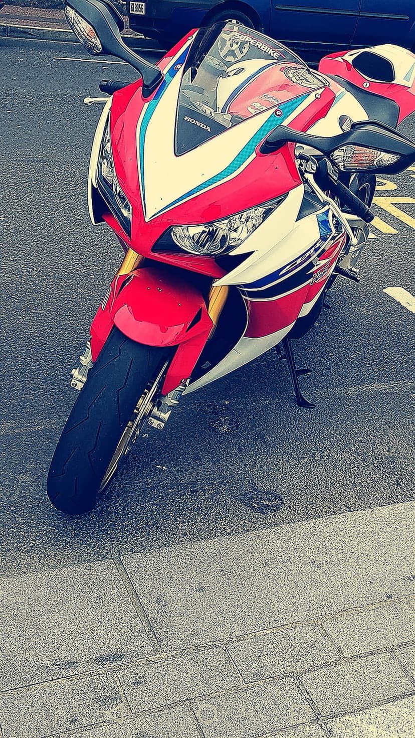 Honda CBR sportbike with red, white, and blue fairings parked on an asphalt street in a front-view perspective.