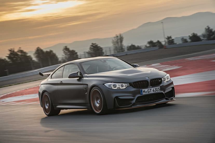 Matte grey sports car with orange accents driving fast on a racetrack during a golden hour sunset.
