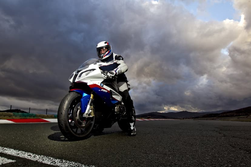 BMW S1000RR sportbike with a rider on a racetrack under dramatic clouds and cinematic lighting.