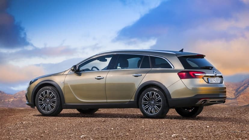 Bronze Opel Insignia Country Tourer wagon on a gravel desert under a sunset sky with blue and orange clouds.