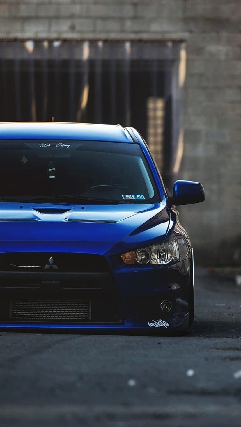 Blue Mitsubishi Lancer Evolution X with a lowered stance and front intercooler parked on urban asphalt.