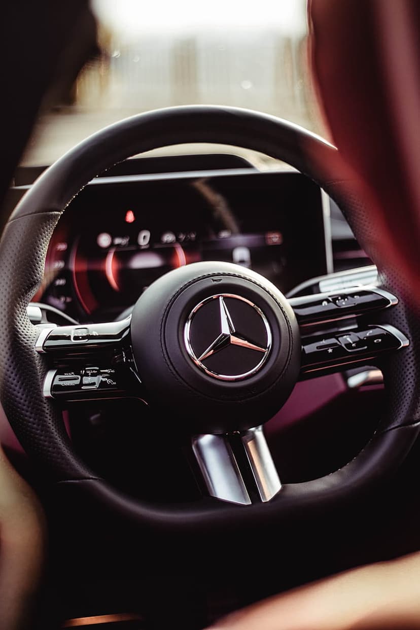 Mercedes steering wheel logo glows against a blurred red digital dashboard in a luxury car cabin wallpaper.