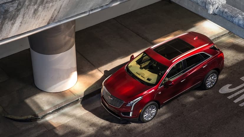 Red Cadillac XT5 SUV parked under a concrete bridge with dramatic sunlight hitting its metallic red paint.