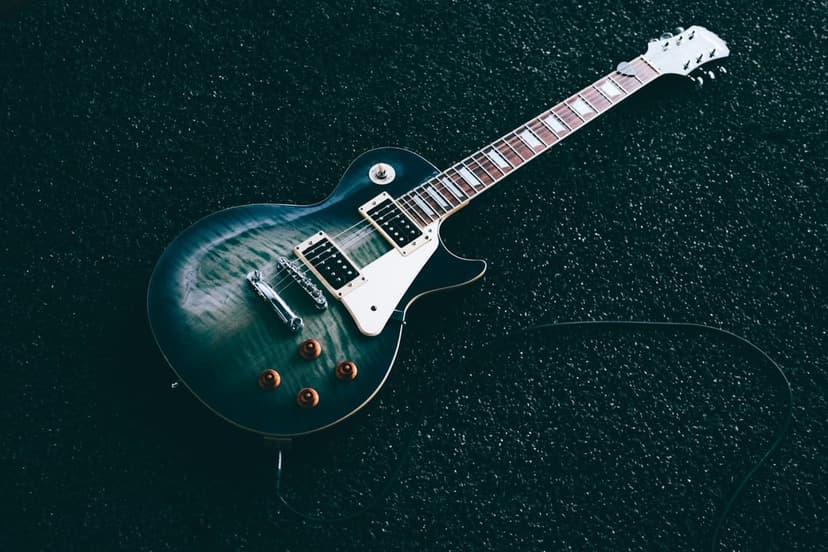 Teal electric guitar with a flame maple top, white pickguard, and coiled cable on a black textured surface.