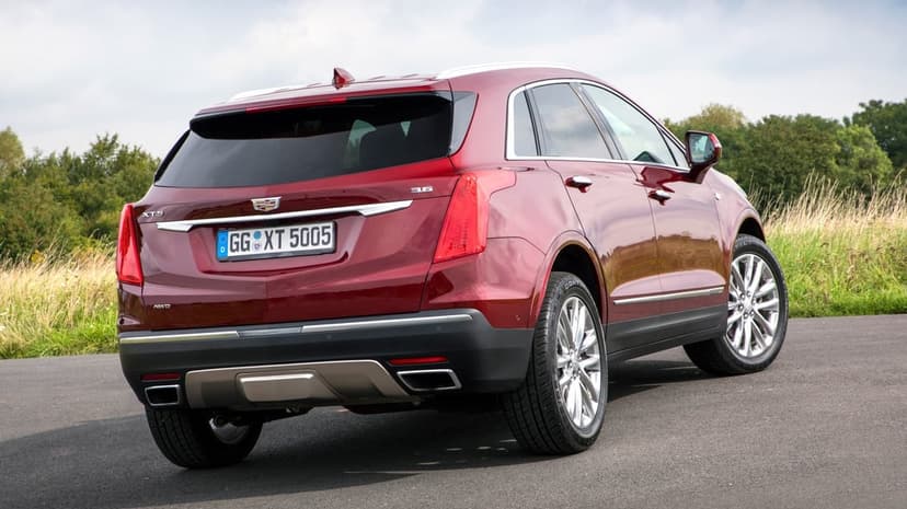 Metallic red Cadillac XT5 luxury SUV parked on a road with green trees and a cloudy sky in the background.