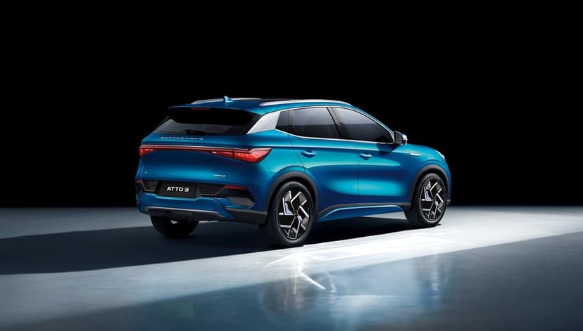 Rear view of a cyan blue electric SUV with glowing LED lights in a dark studio with bright floor reflections.