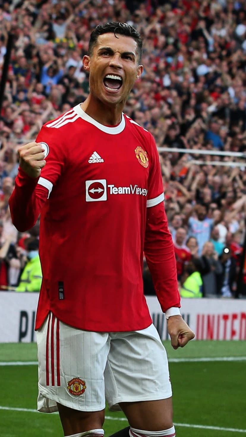 Cristiano Ronaldo shouts in celebration wearing a red Manchester United jersey with a blurred crowd in the background.