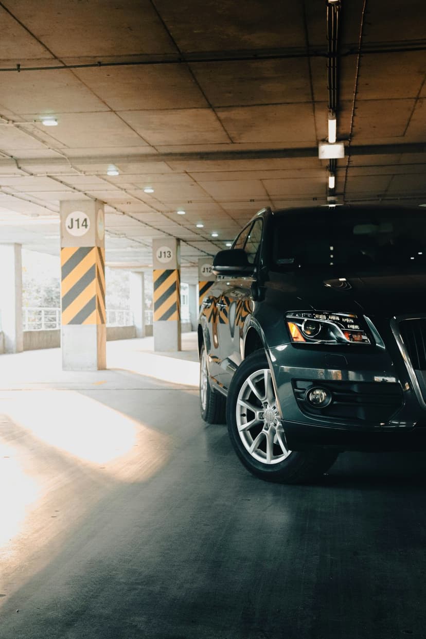 Dark SUV parked in a concrete garage with sunlight hitting alloy wheels and striped pillars J13 and J14.