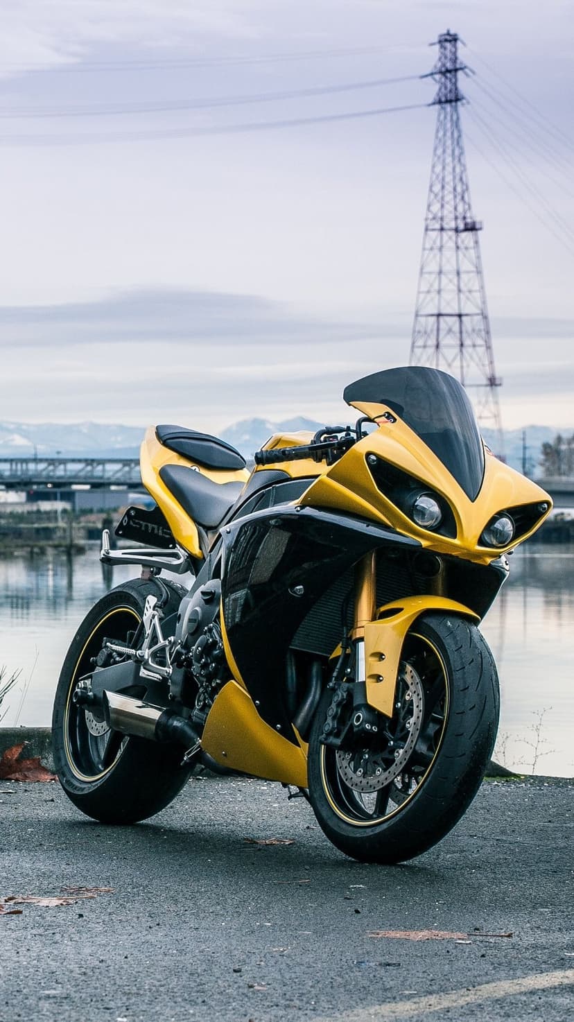 Yellow and black sportbike parked on asphalt near a river with a power tower and bridge in the background.