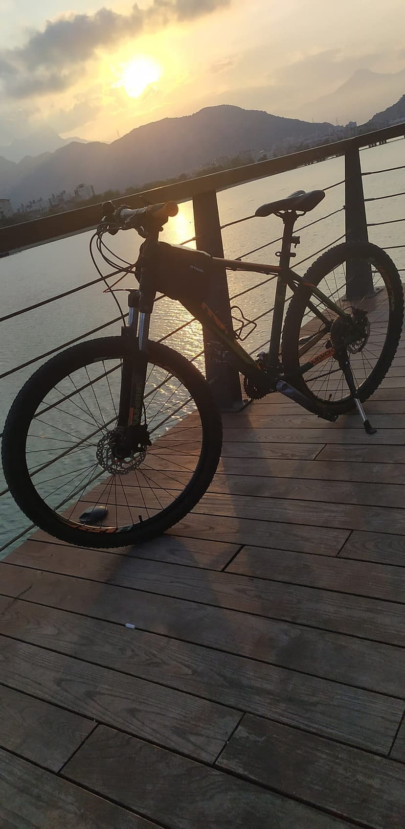 Mountain bike parked on a rustic timber deck during a vibrant sunset with peaks reflecting in the water.