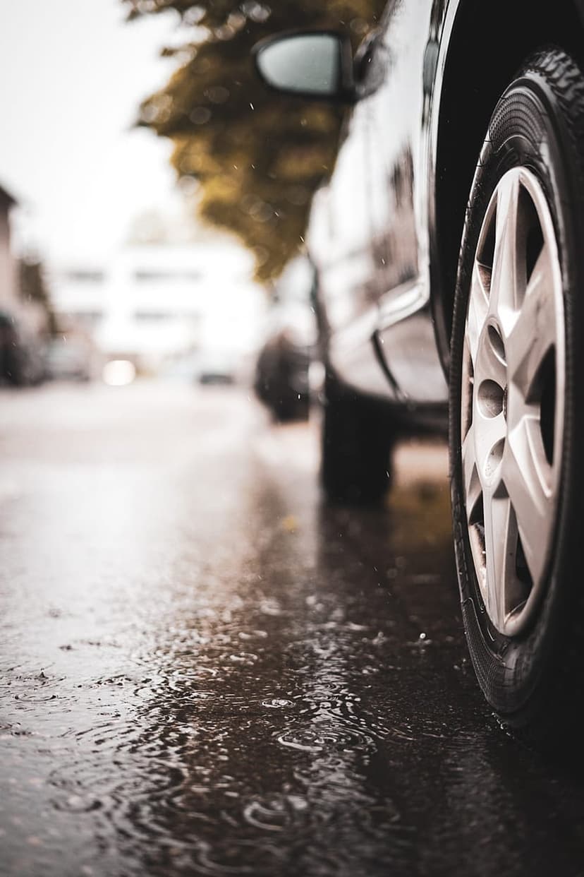 Car tire tread on a wet asphalt road with raindrops creating ripples and a soft bokeh background.