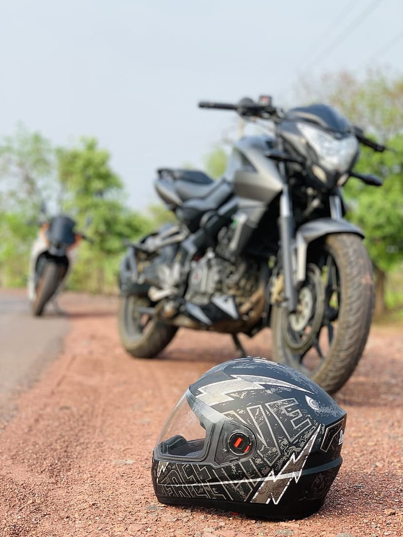 Black motorcycle and full-face helmet with white graphics rest on a dirt road against a blurred natural background.
