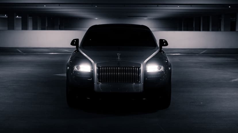 Front view of a dark luxury car with glowing headlights and a silver grille in a dim underground garage.