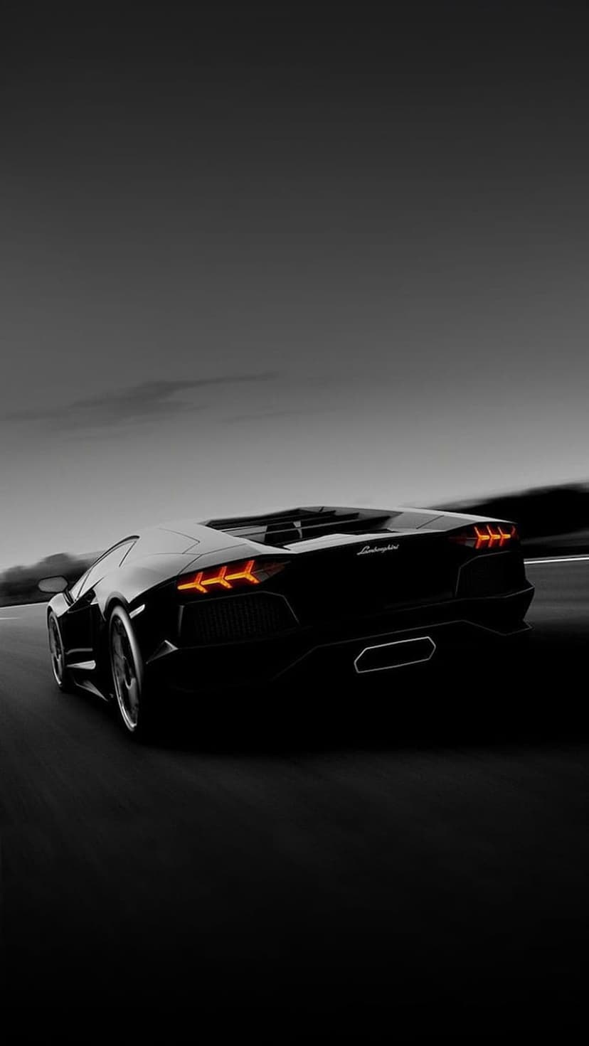 Black Lamborghini Aventador with orange taillights driving at high speed on a dark road during dusk.