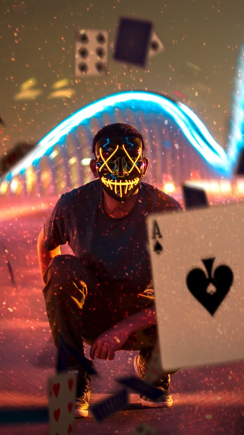 Masked person with a glowing X face squats on a road as playing cards and dice float against a neon bridge.