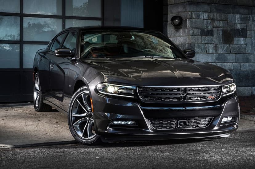 Dark gray Dodge Charger muscle car parked by a stone wall with glowing headlights and a polished metallic exterior.