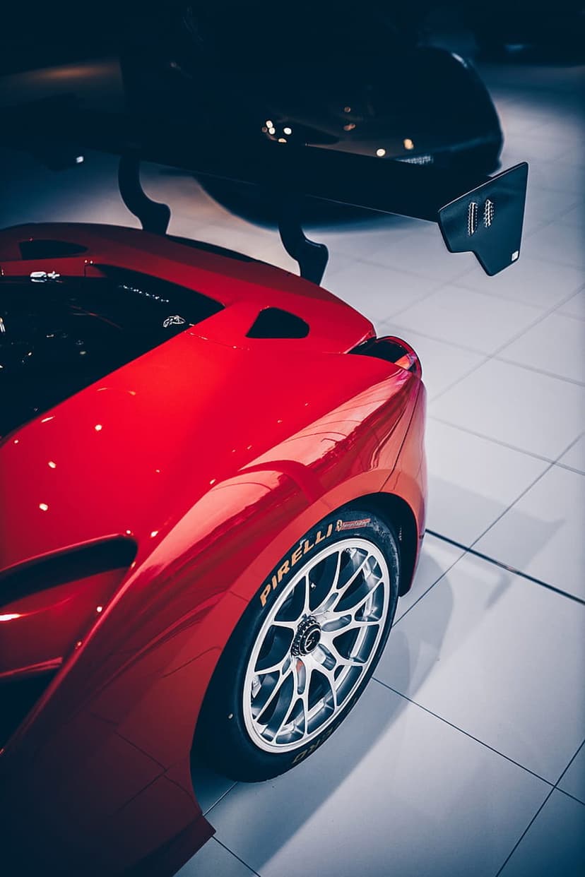 Red supercar rear fender and silver alloy wheel featuring a performance tire and black aerodynamic wing detail.