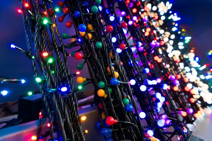 Vibrant red, green, and blue LED holiday lights are tightly coiled around a dark textured electrical cable.