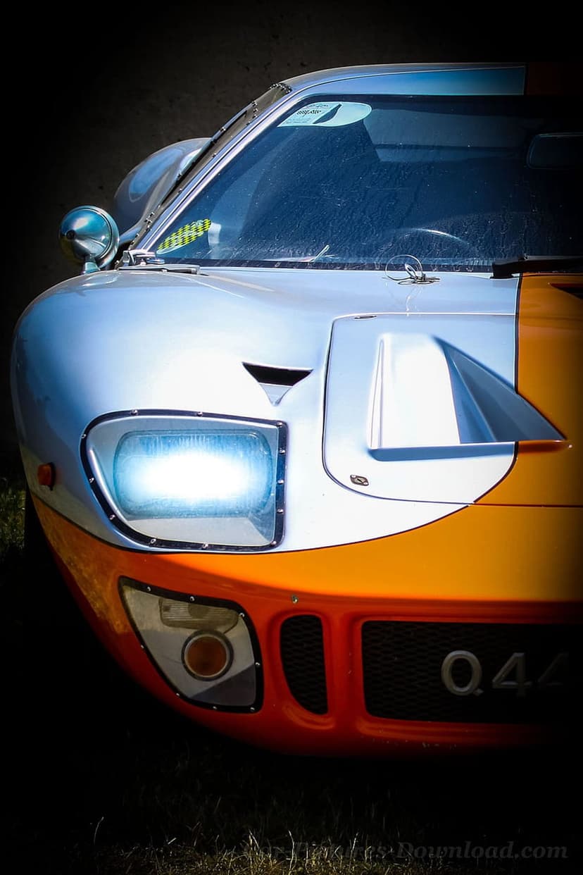 Ford GT40 headlight and silver bodywork with orange racing stripes in a detailed front-angle close-up view.