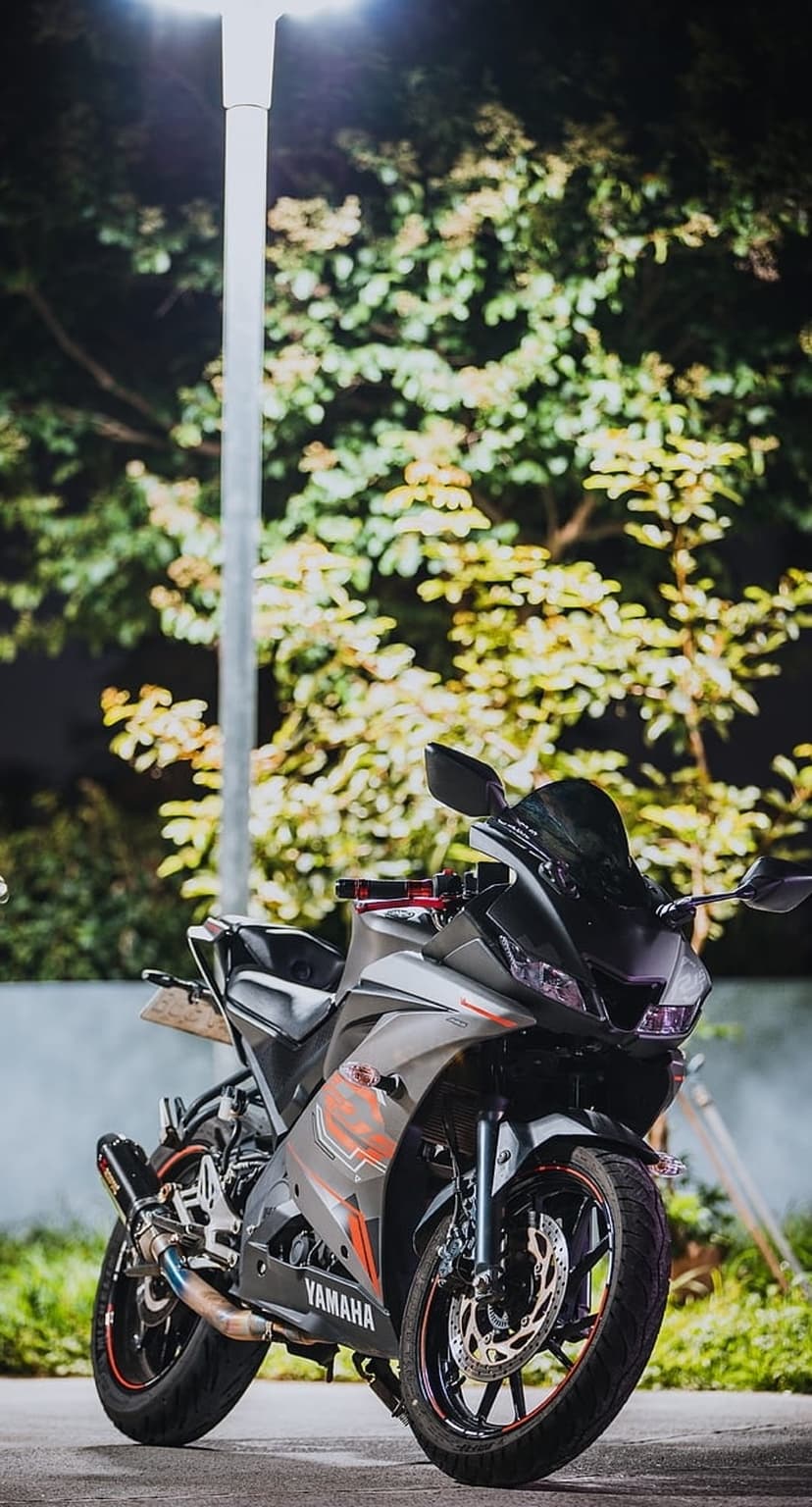 Yamaha sportbike with orange accents parked under a glowing streetlight with blurred green and yellow tree leaves