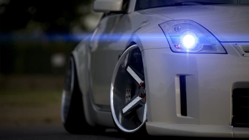 Close-up of a stanced white Nissan 350Z with deep-dish wheels and a bright blue glowing headlight lens flare.