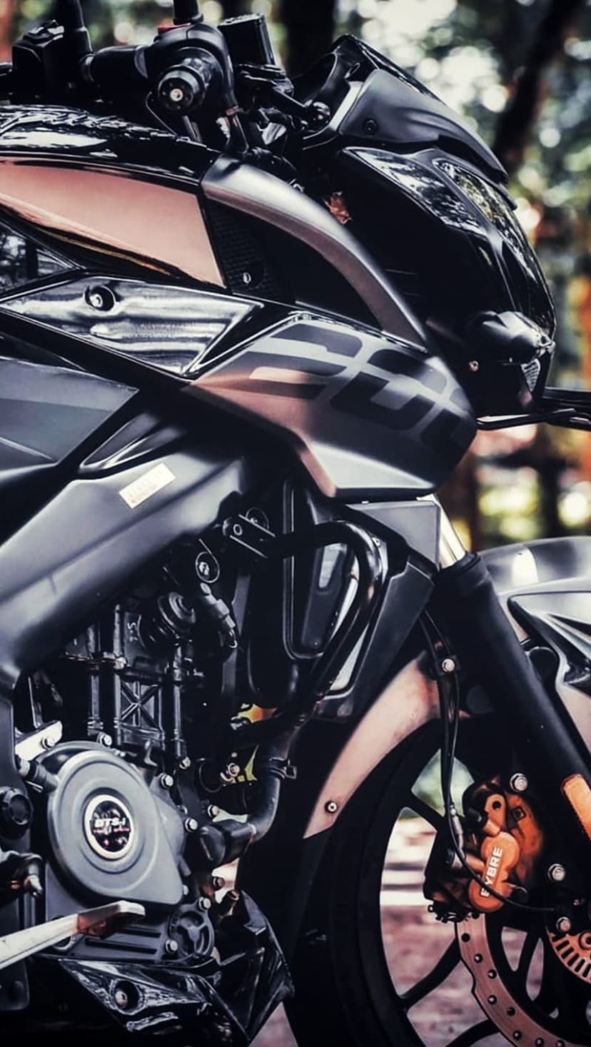 Black and copper motorcycle engine showcasing brushed metal textures and mechanical parts against a blurred park.