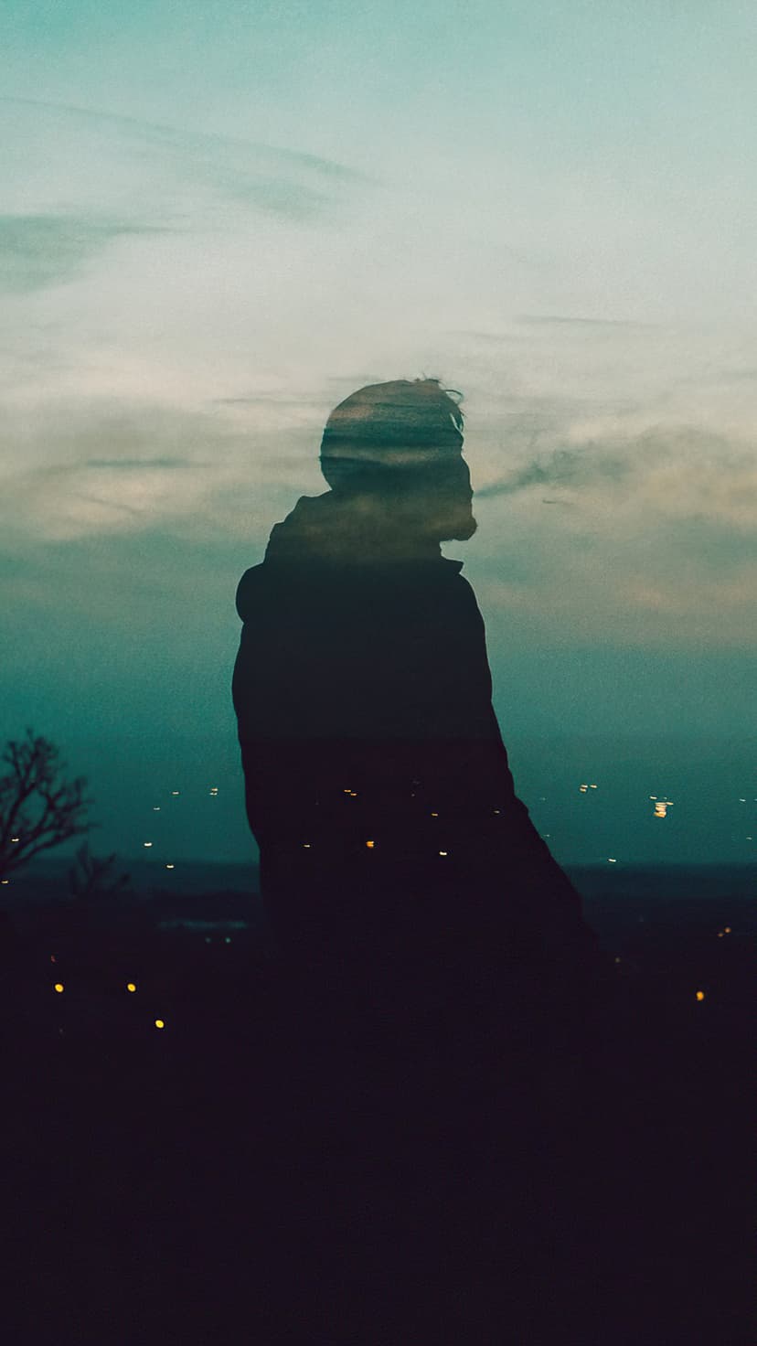 Human profile silhouette filled with a dramatic teal sky and city lights in a vertical double exposure effect.