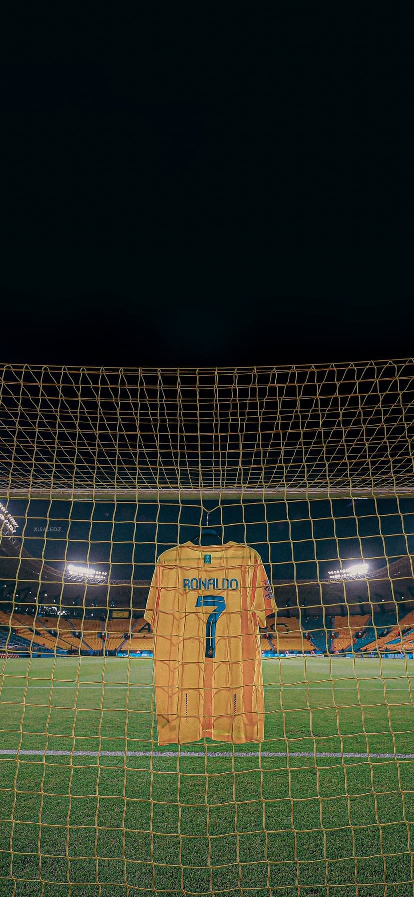 Yellow soccer jersey with number 7 hangs in a goal net at a lit stadium at night with blurred grandstands.