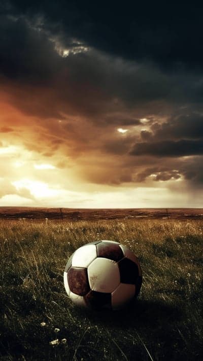 Soccer ball on grass under stormy sky
