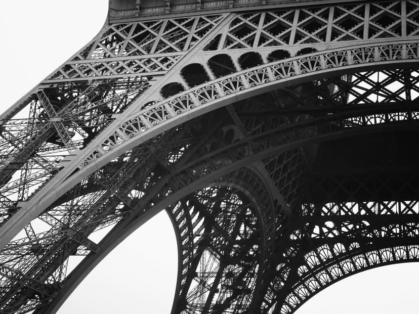 Eiffel Tower iron latticework and curved steel supports viewed from below in a high-contrast monochrome style.