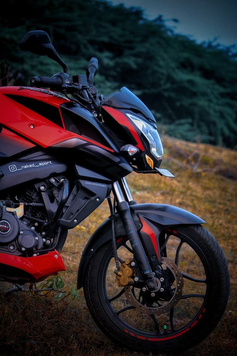 Red and black sportbike parked on a grassy slope with focused details on the front wheel and suspension system.