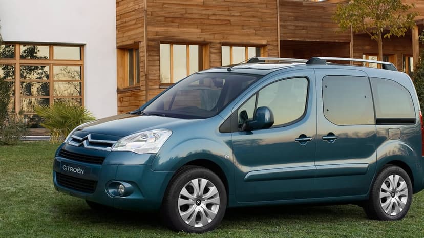 Teal Citroen Berlingo Multispace parked on grass in front of a modern wooden house during golden hour.