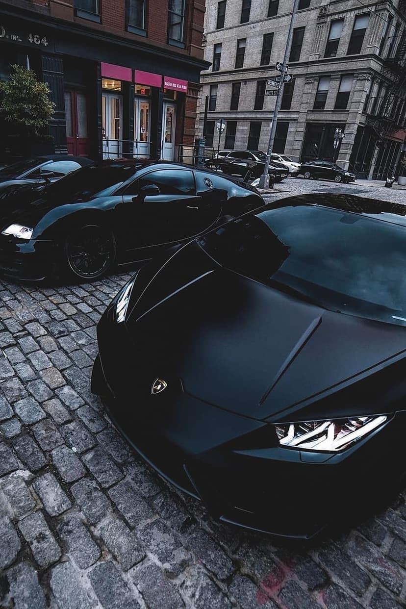Lamborghini and Bugatti parked on a wet cobblestone street at night in front of historic European buildings.