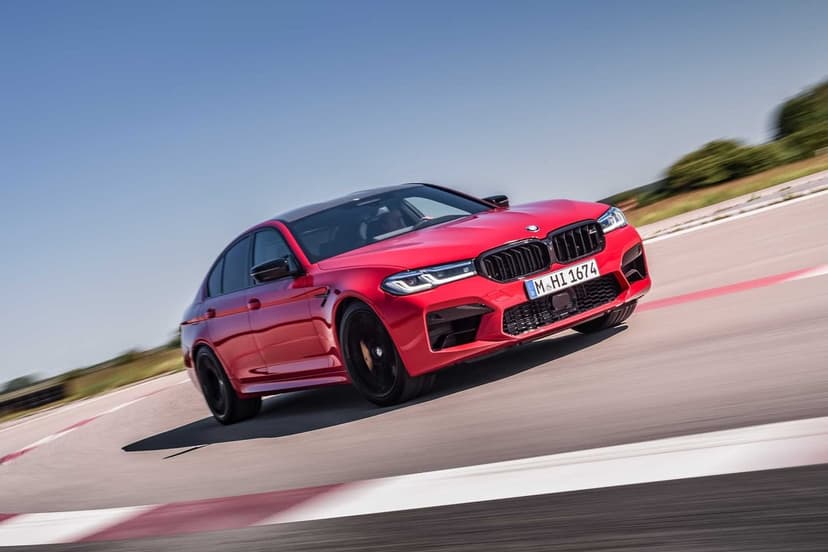 Red BMW M5 Competition driving at high speed on a racetrack with motion blur under a clear blue sky.