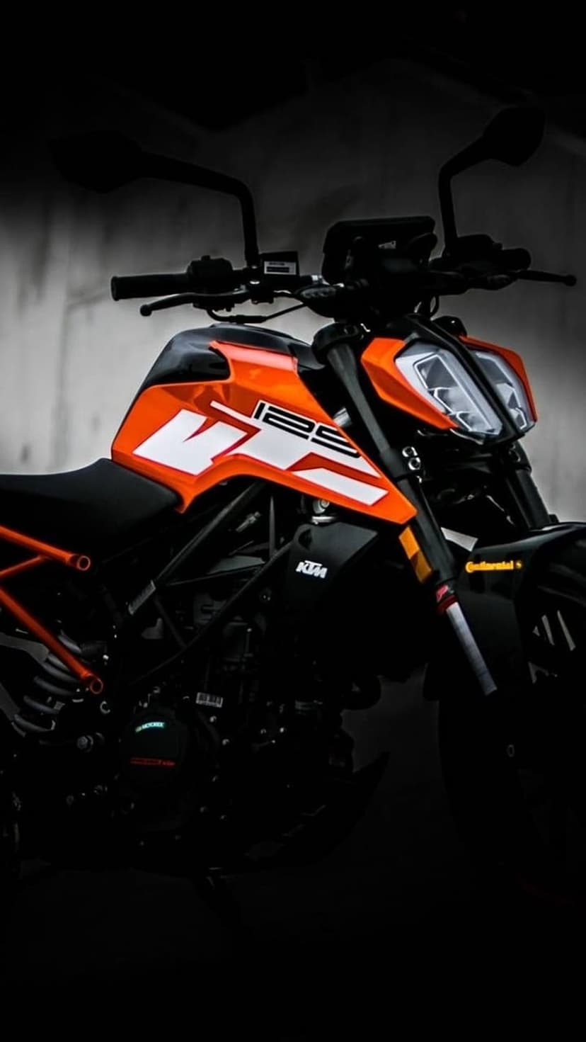 KTM 125 Duke motorcycle with orange accents emerges from deep shadows in a low-key lighting vertical shot.