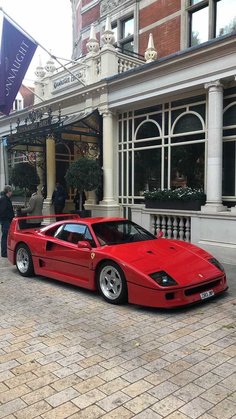 Red Ferrari F40 supercar parked on a cobblestone driveway in front of an elegant historic hotel building.