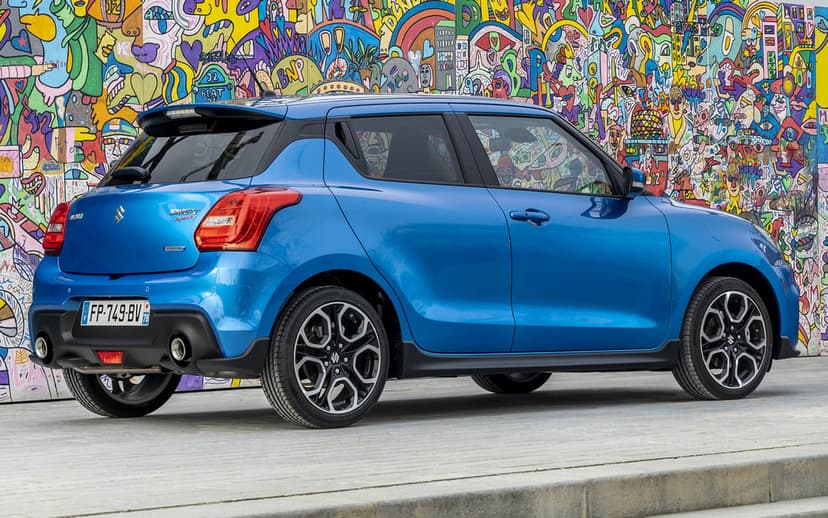 Blue Suzuki Swift Sport parked in profile against a vibrant graffiti mural wall with urban street art designs.