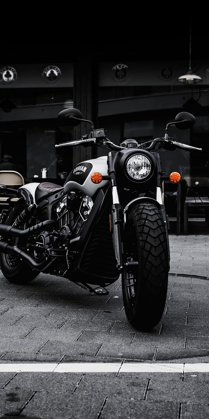 Indian motorcycle with a round headlight and dual exhaust pipes parked on a textured cobblestone city street.