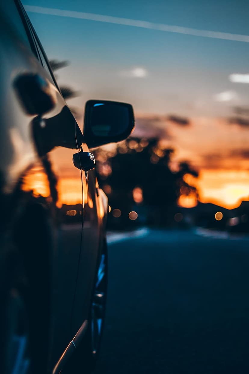 Car side mirror reflecting a vibrant orange and blue sunset with blurred street lights in the background.