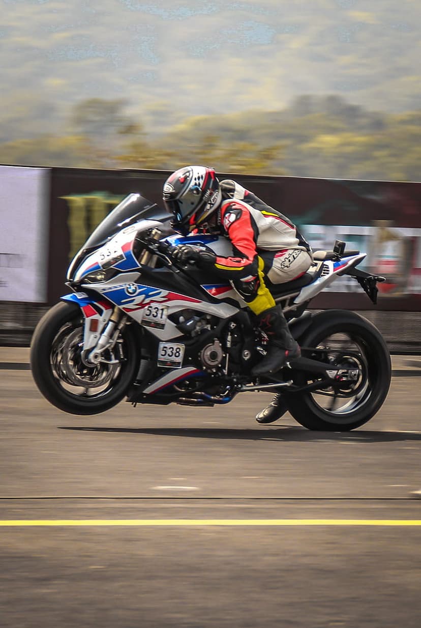 BMW S1000RR rider in full racing gear executes a vertical wheelie on a race track with background motion blur.