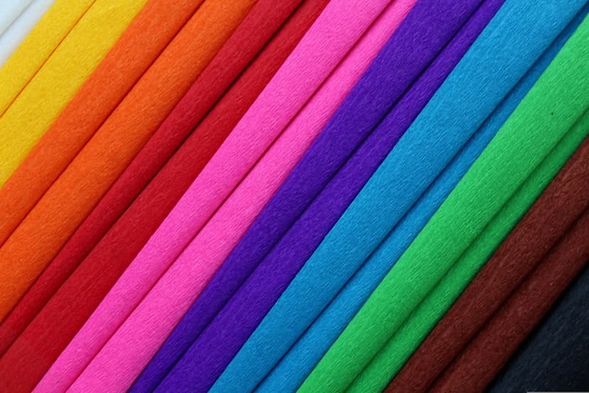 Rainbow crepe paper rolls stacked diagonally in a close-up view showing fine crinkled textures and vivid hues.