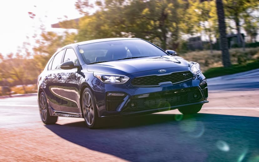 Dark blue Kia Forte GT sedan driving on a sunlit road with golden hour lens flare and motion blur.