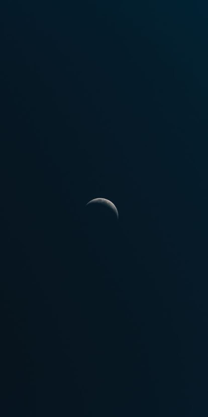 Slender crescent moon glowing softly against a dark blue gradient sky with subtle atmospheric haze and depth.