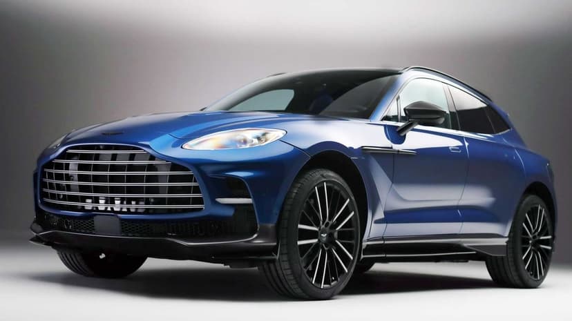 Metallic blue Aston Martin DBX luxury SUV in a studio with a chrome grille and black multi-spoke alloy wheels.