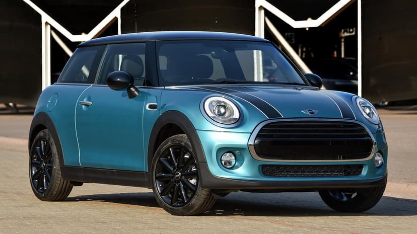 Teal MINI Cooper with black racing stripes and wheels parked on a paved surface under bright sunlight.