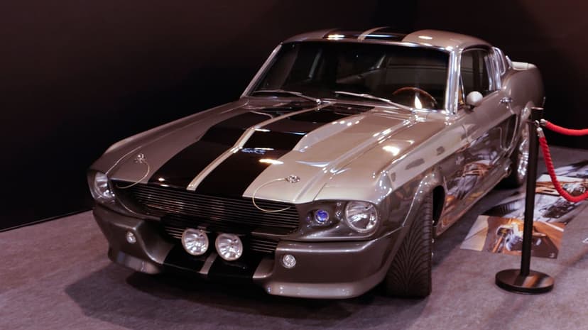 Silver 1967 Shelby Mustang Eleanor with black racing stripes and fog lights in a studio setting.