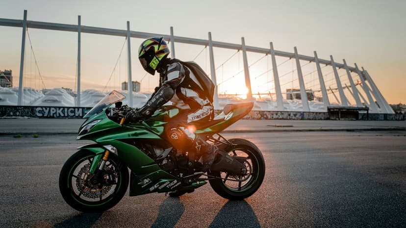 Motorcyclist in black gear riding a neon green sportbike past a modern stadium during a golden sunset.