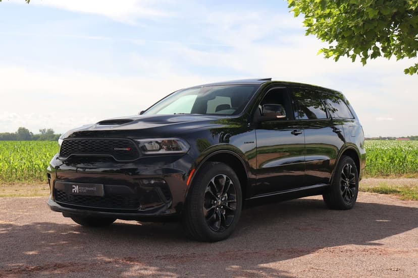 Black Dodge Durango SUV parked on a dirt road next to a cornfield under a bright sunny sky with a green tree.